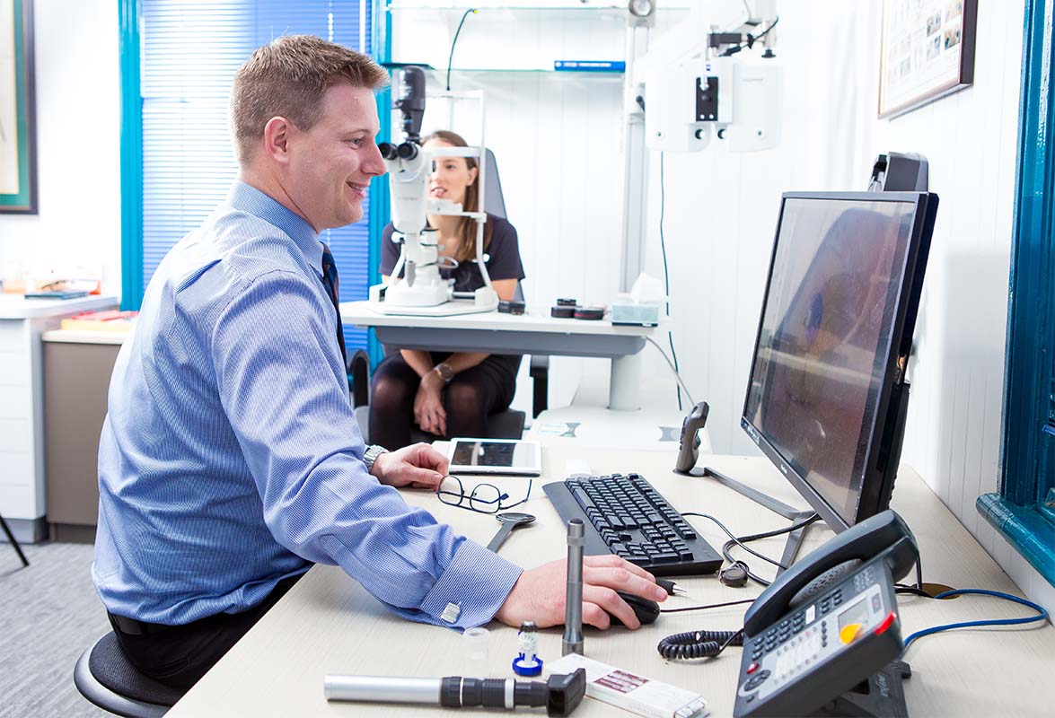 Heron Eyecare team member looking at monitor while testing patients eyes